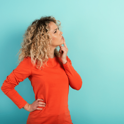 Woman in long sleeved, red shirt with one hand on hip and the other rubbing her chin in thought, representing braces vs aligners