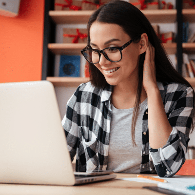 Woman wearing flannel shirt and black glasses, smiling, and working on a laptop computer, representing minera orthodontics' new website