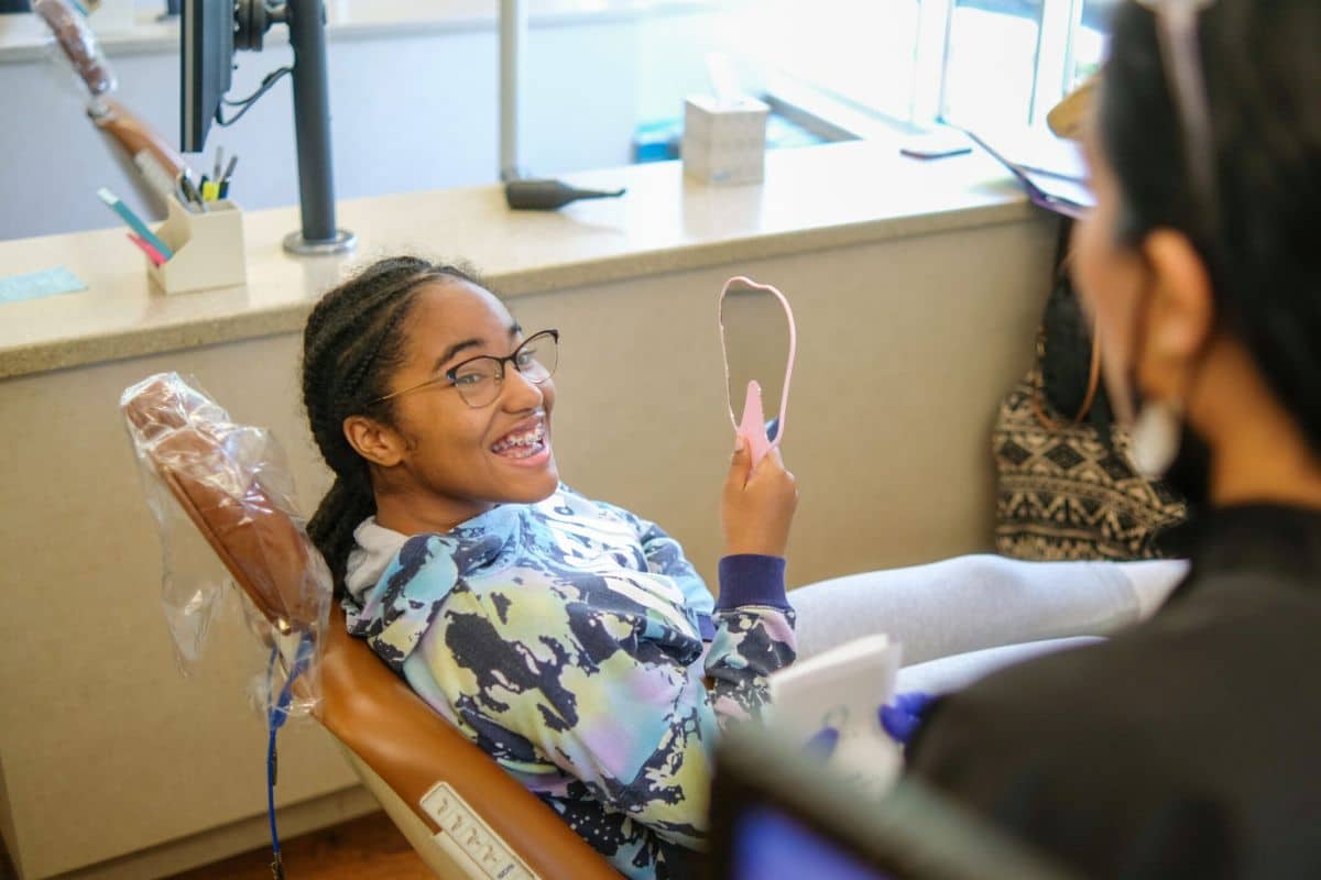 Teen patient with braces smiling while holding a mirror during an orthodontic appointment at minera orthodontics in warrenton, va.