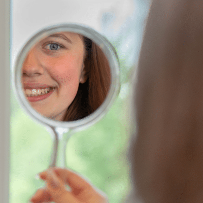 Teenage girl looking at herself in a small mirror, representing best clear aligner options